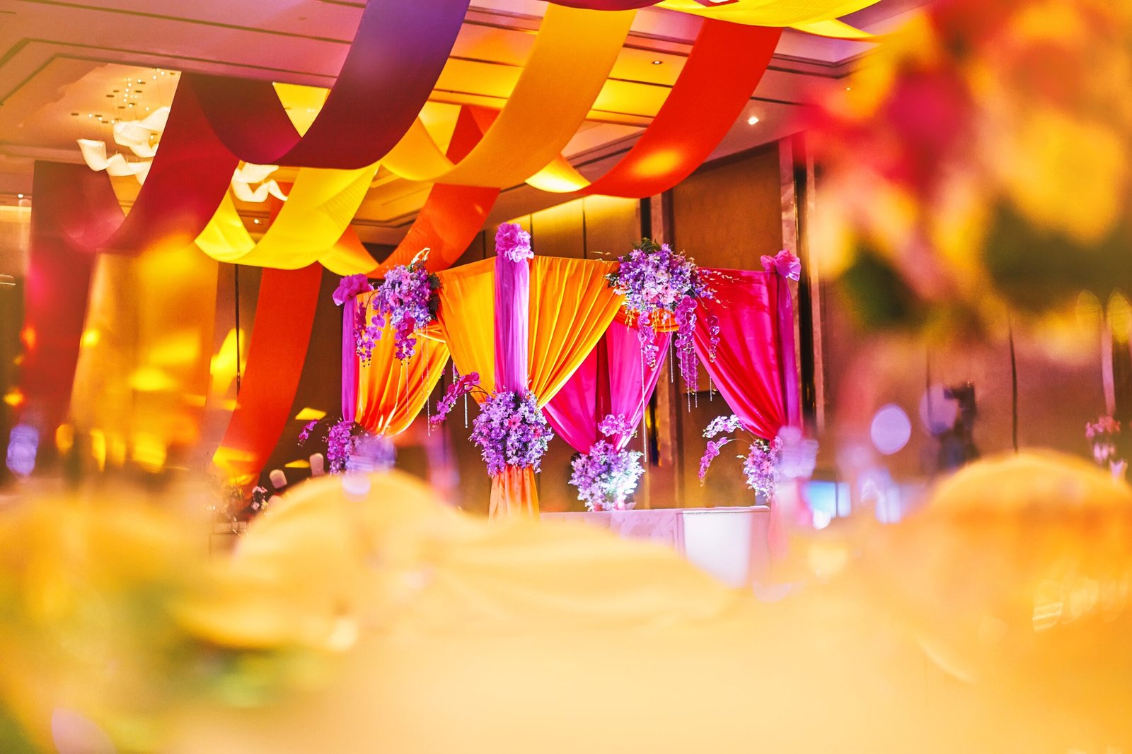 Selective focus on the colorful stage decoration with bright shade of color for bride and groom in the sangeet night of traditional indian wedding party celebration with blurry foreground